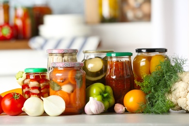 Photo of Fresh vegetables and jars of pickled products on wooden table