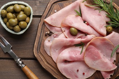 Photo of Slices of delicious ham with rosemary and olives served on wooden table, flat lay