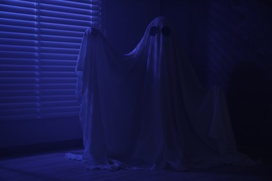 Photo of Creepy ghost. Woman covered with sheet near window in blue light