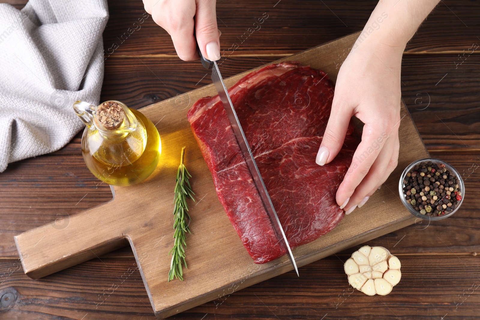 Photo of Woman cutting fresh raw beef steak at wooden table, top view