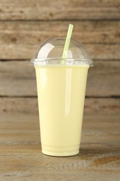 Photo of Plastic cup of tasty smoothie on wooden table