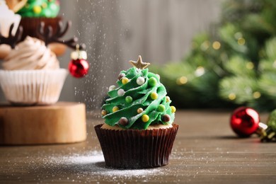 Sprinkling powdered sugar on Christmas tree shaped cupcake at wooden table