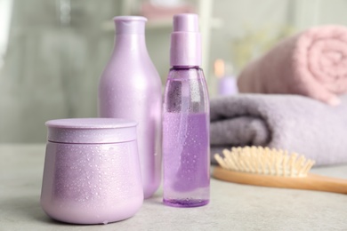 Photo of Set of hair care cosmetic products covered with water drops on light grey stone table in bathroom