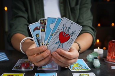 Photo of Fortune teller with tarot cards at grey table indoors, closeup