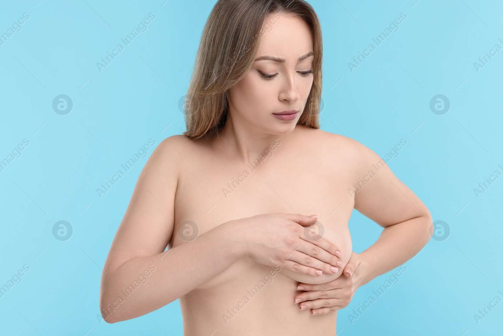 Photo of Mammology. Naked young woman doing breast self-examination on light blue background