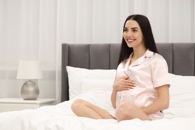 Happy pregnant woman on bed at home, space for text