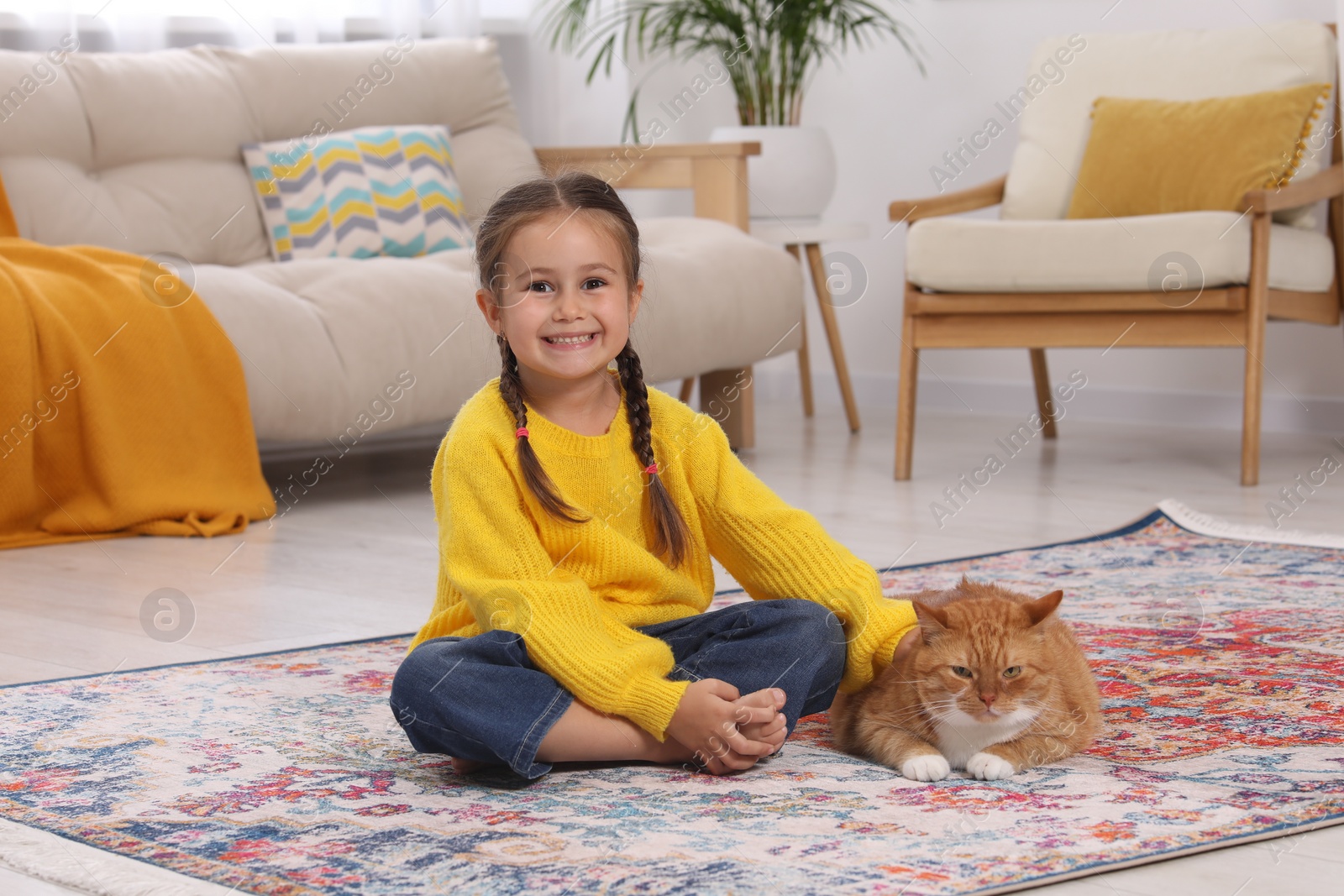 Photo of Happy little girl and cute ginger cat on carpet at home