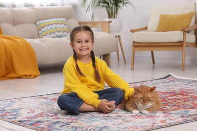 Happy little girl and cute ginger cat on carpet at home