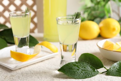 Photo of Tasty limoncello liqueur and green leaves on light textured table, closeup