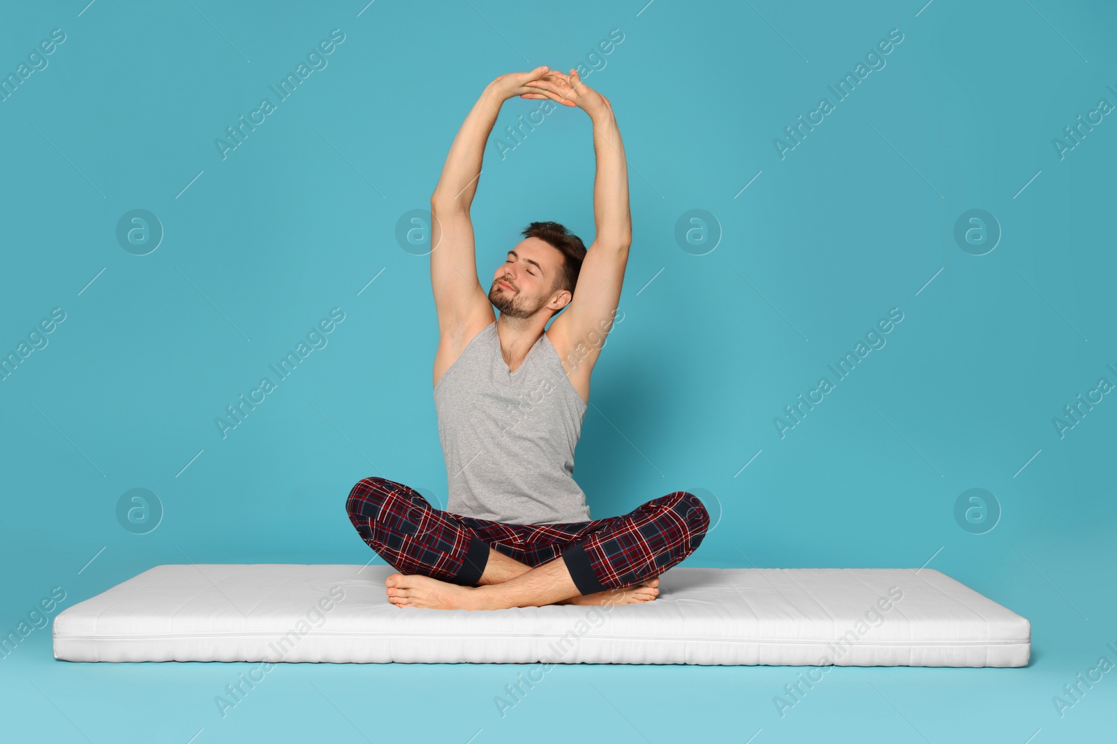 Photo of Man stretching on soft mattress against light blue background