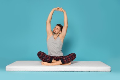 Photo of Man stretching on soft mattress against light blue background