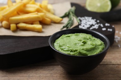 Photo of Serving board with french fries, avocado dip, rosemary and lime served on wooden table, closeup