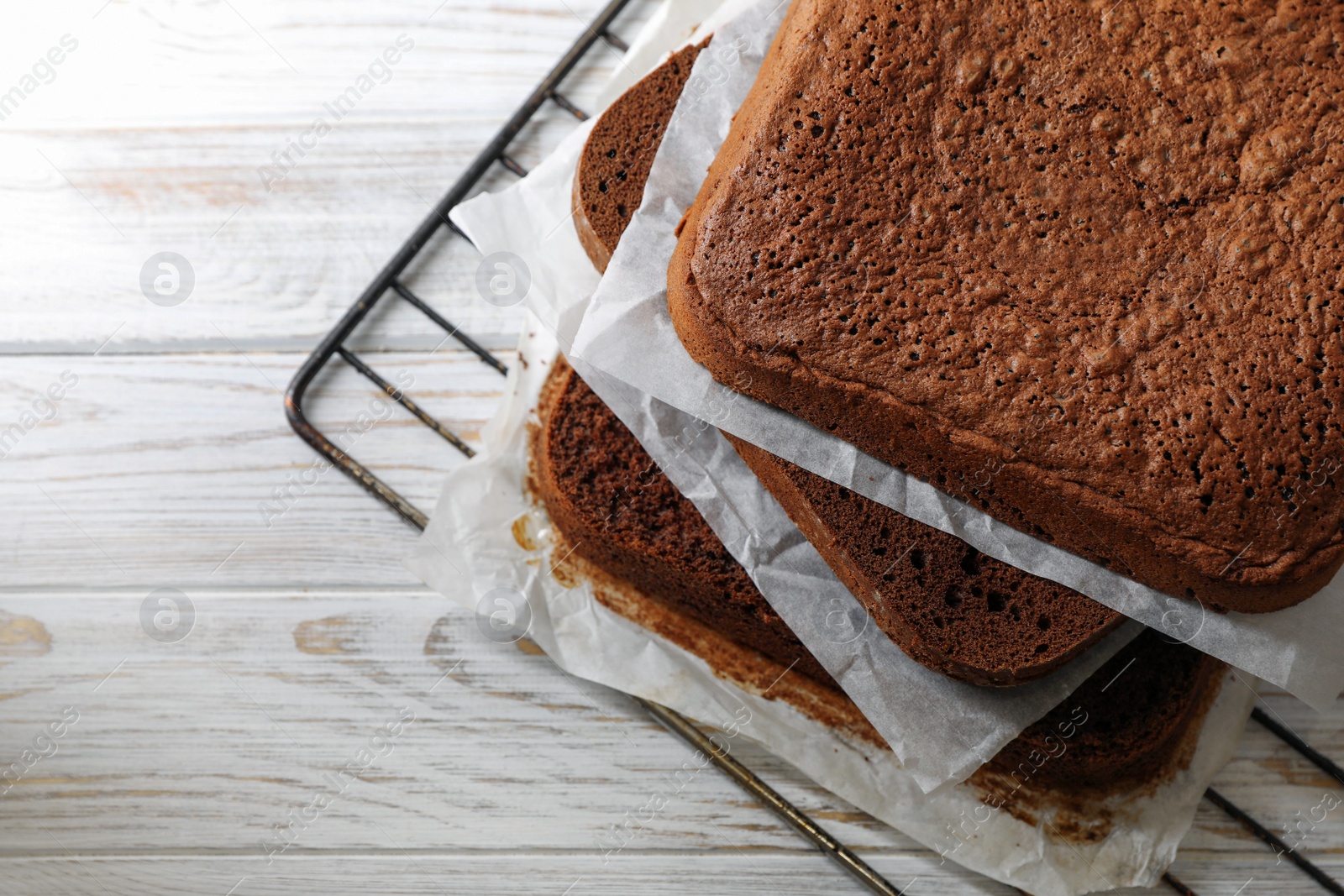 Photo of Layers of homemade chocolate sponge cake on white wooden table, closeup. Space for text