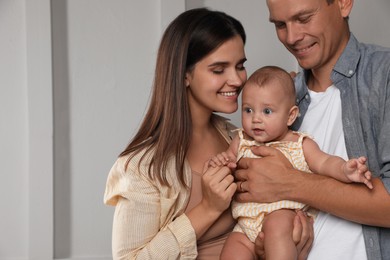 Happy family. Couple with their cute baby near light wall