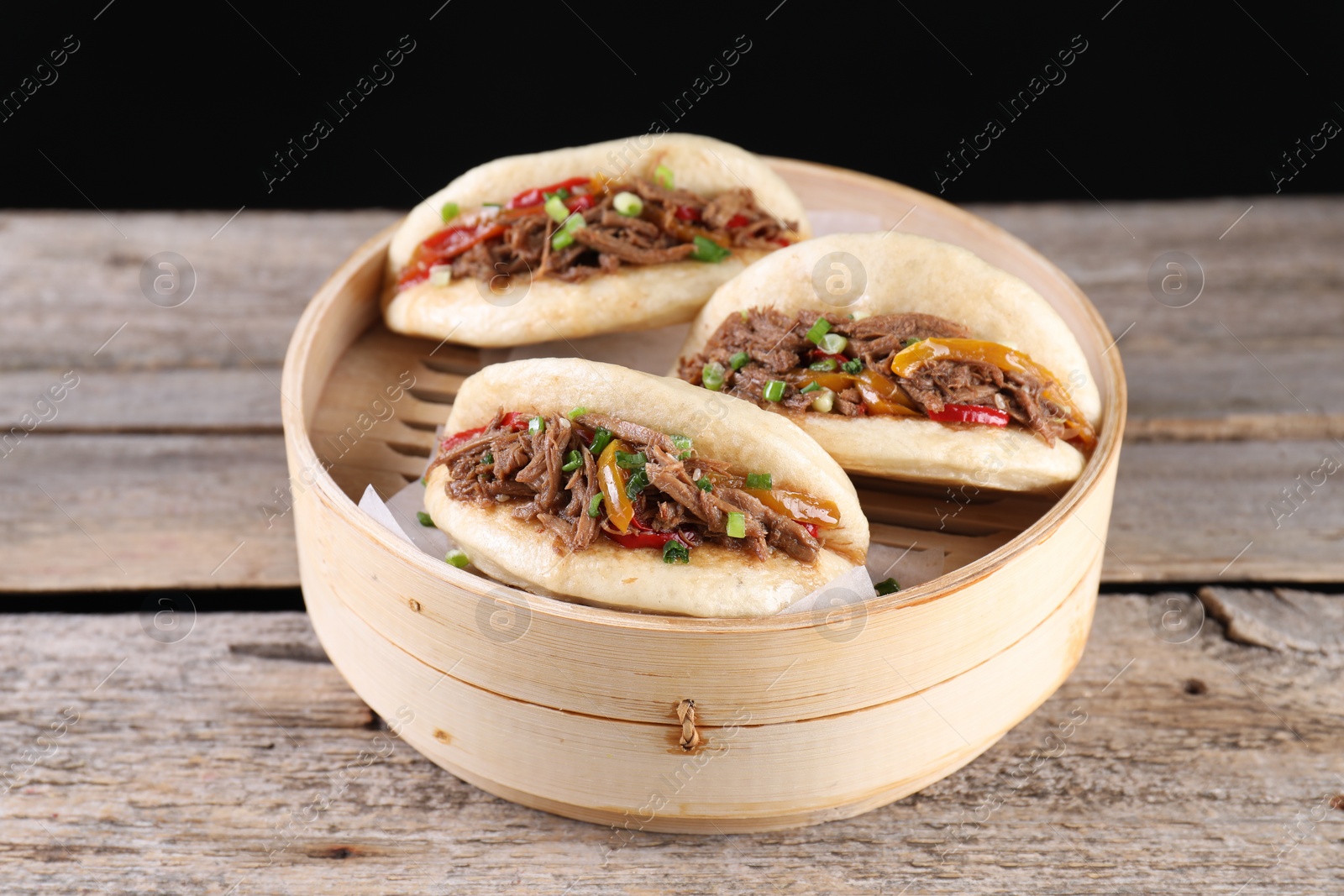 Photo of Delicious gua bao in bamboo steamer on wooden table