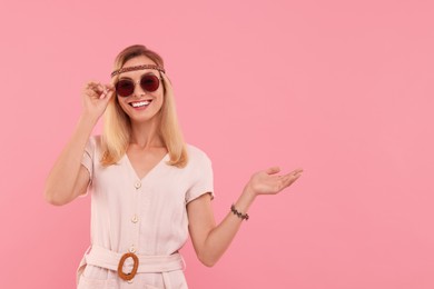 Photo of Portrait of smiling hippie woman in sunglasses on pink background. Space for text