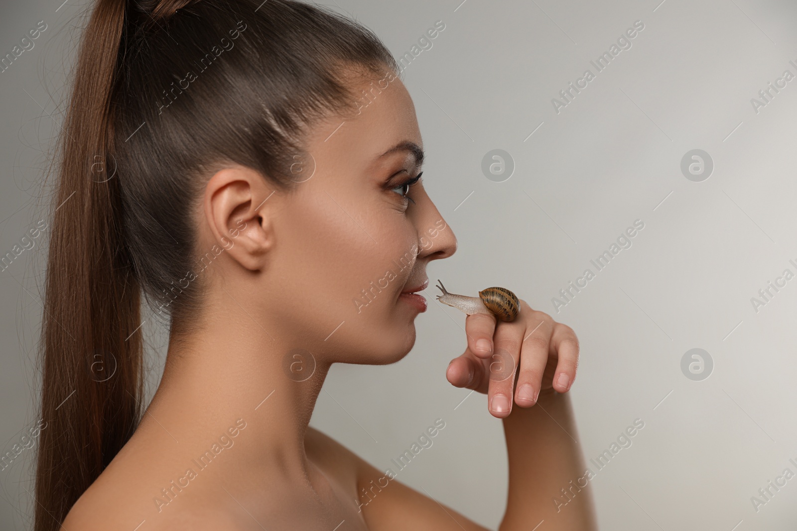 Photo of Beautiful young woman with snail on her hand against grey background. Space for text