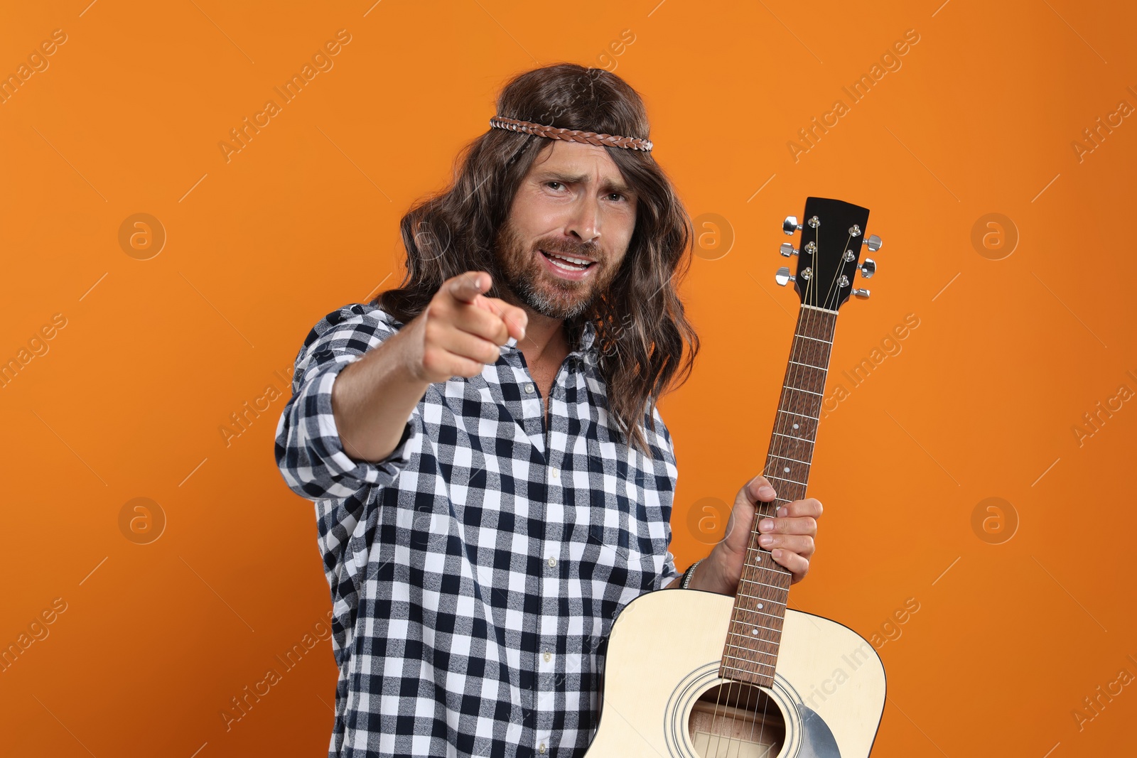 Photo of Hippie man with guitar pointing at camera on orange background