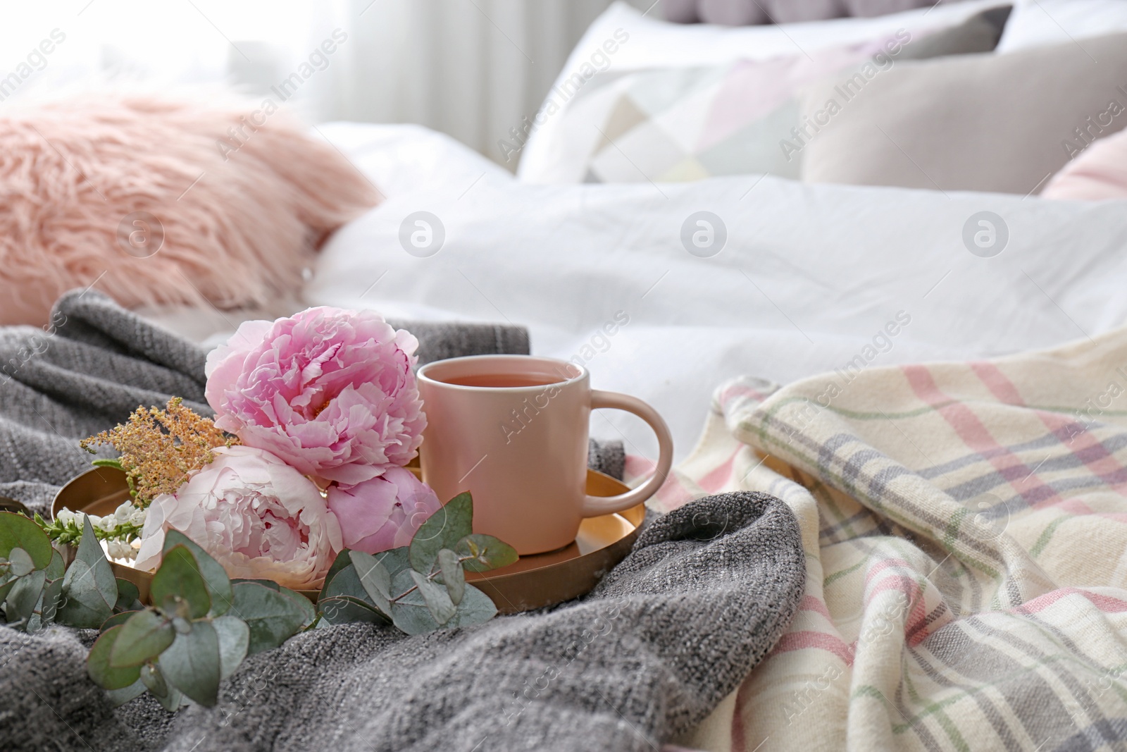 Photo of Cup of drink and bouquet on bed with pillows in room