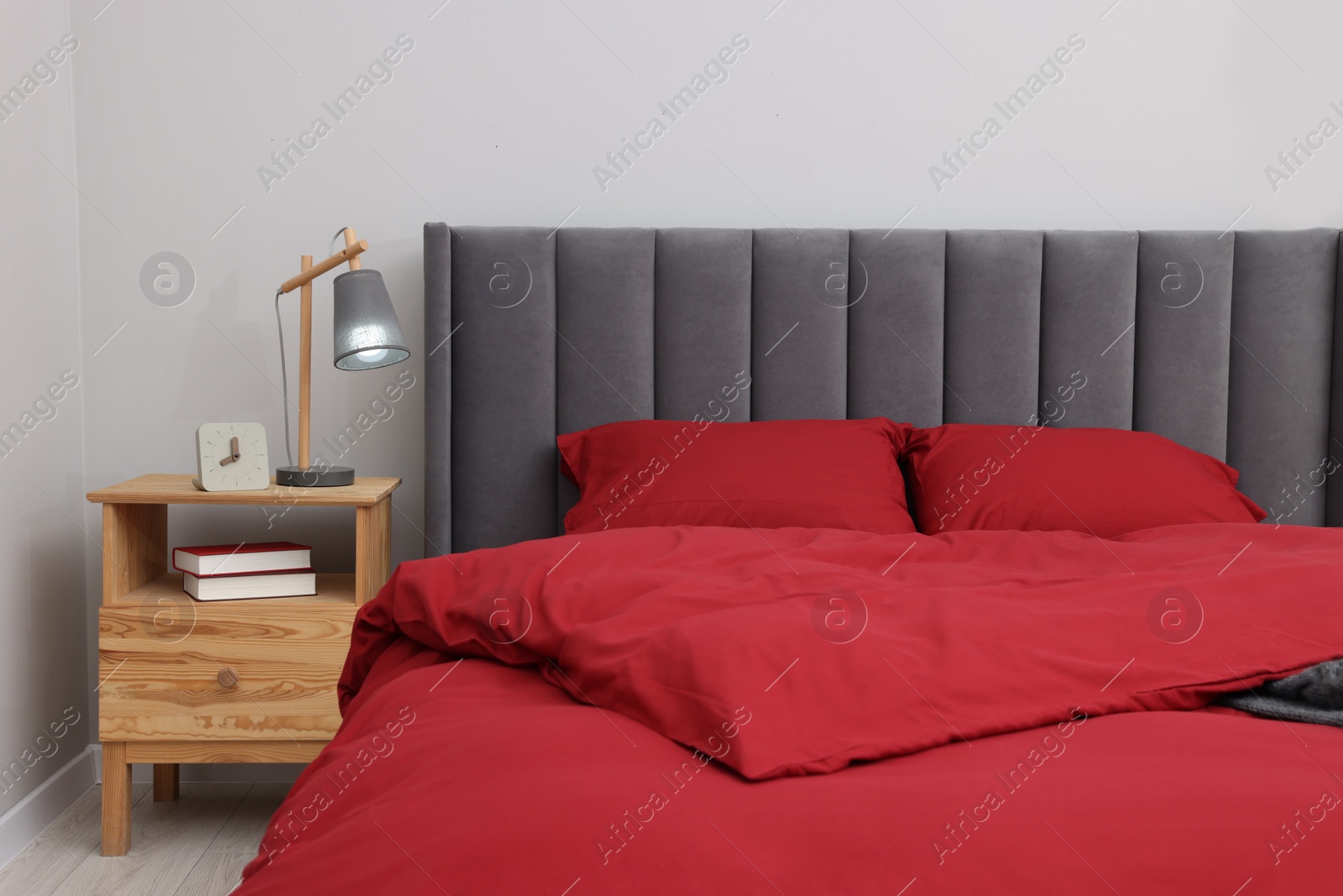 Photo of Comfortable bed, lamp, alarm clock and books on wooden bedside table in bedroom. Interior design