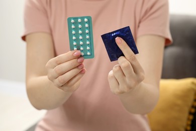 Photo of Woman holding condom and contraceptive pills on blurred background, closeup. Choosing birth control method