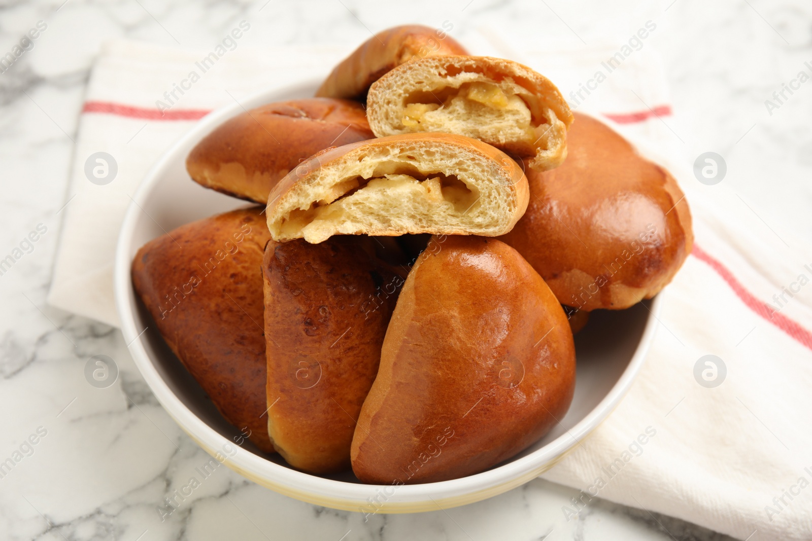 Photo of Delicious baked apple pirozhki in bowl on white marble table