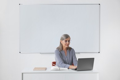 Photo of Professor giving lecture while using laptop at desk in classroom