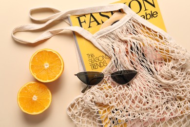 Photo of String bag, magazine, sunglasses and halves of orange on beige background, top view