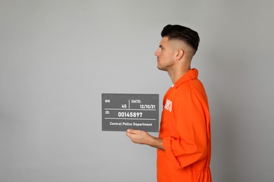 Photo of Mug shot of prisoner in orange uniform with board on grey background, side view