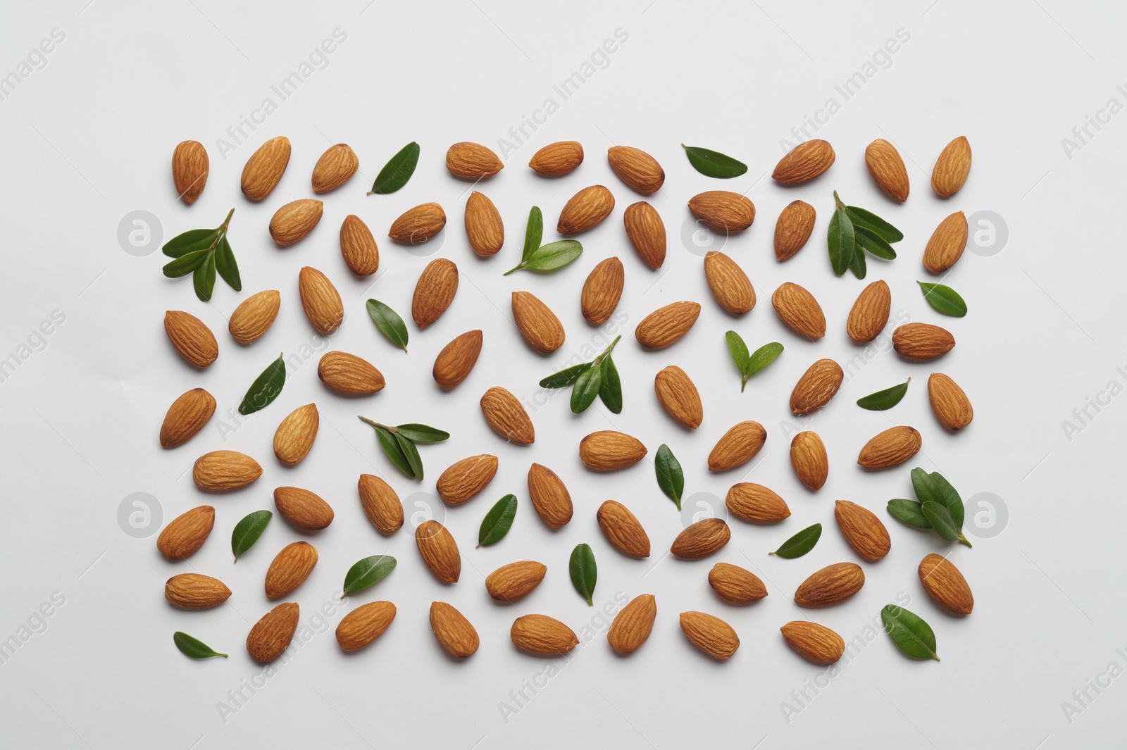 Photo of Delicious almonds and fresh leaves on white background, flat lay