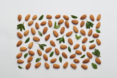 Delicious almonds and fresh leaves on white background, flat lay
