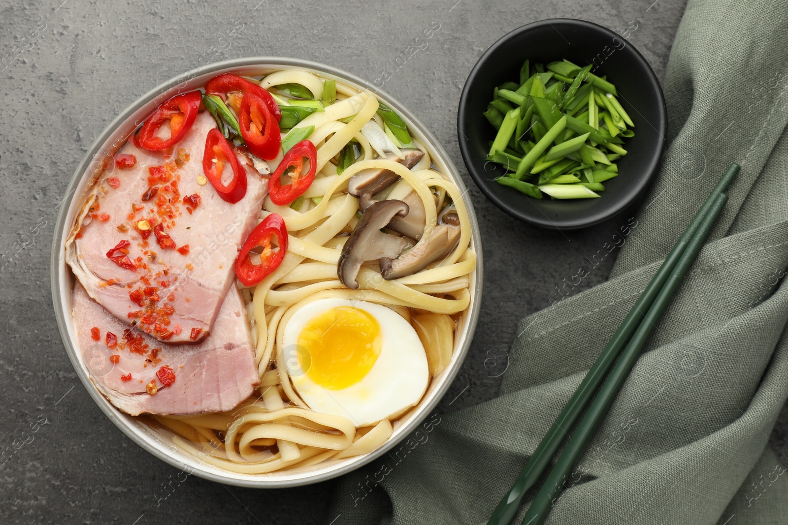 Photo of Delicious ramen in bowl served on grey textured table, flat lay. Noodle soup