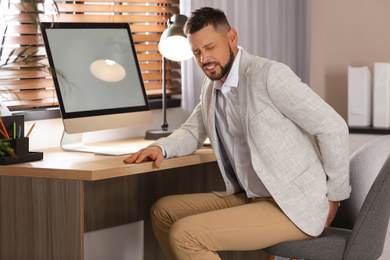 Photo of Man suffering from hemorrhoid at workplace in office