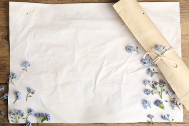 Beautiful forget-me-not flowers and sheets of old parchment paper on wooden table, top view