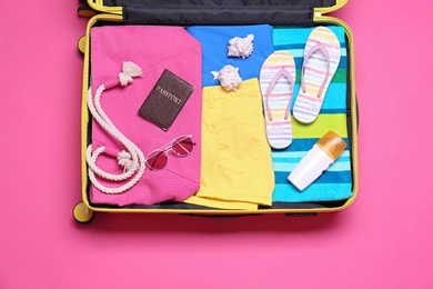 Photo of Open suitcase with beach objects on pink background, top view