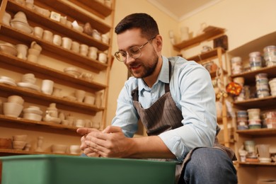 Photo of Man crafting with clay on potter's wheel in workshop, low angle view