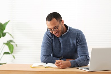 Smiling African American man writing in notebook at wooden table