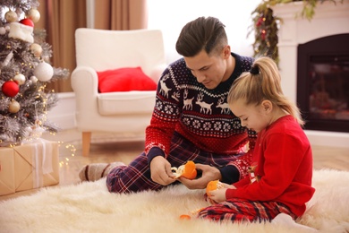 Photo of Father with little daughter peeling tangerines in room decorated for Christmas