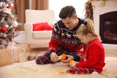 Father with little daughter peeling tangerines in room decorated for Christmas