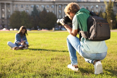 Male photographer taking photo of young woman with professional camera on grass outdoors