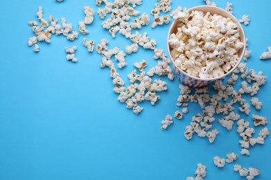 Paper bucket with delicious popcorn on light blue background, flat lay. Space for text