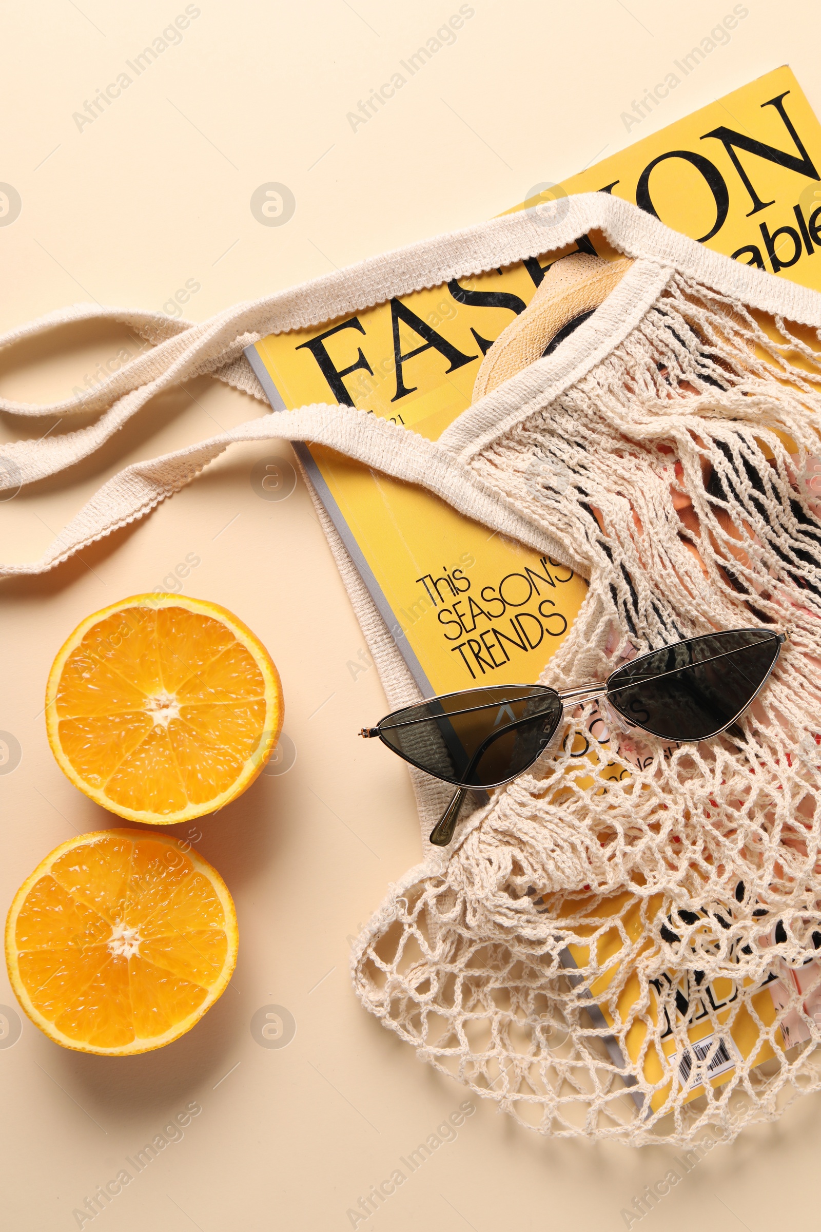 Photo of String bag, magazine, sunglasses and halves of orange on beige background, top view