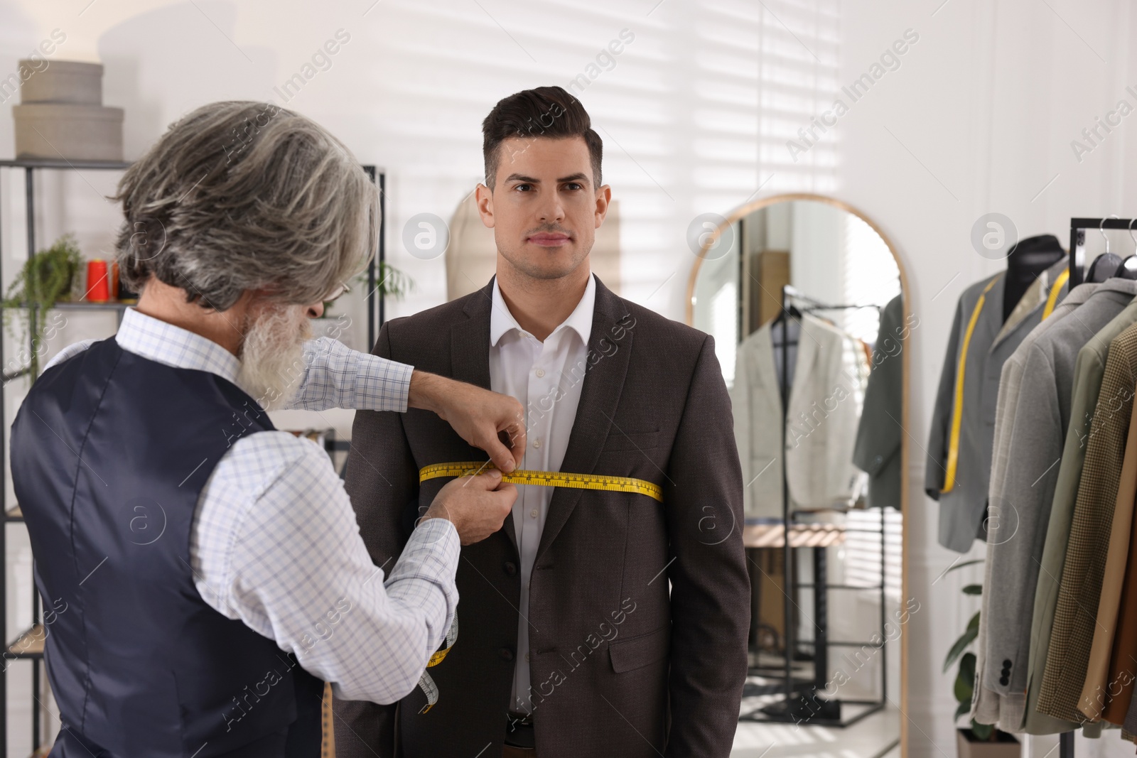 Photo of Professional tailor measuring client's chest circumference in atelier