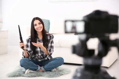 Photo of Young blogger with hair curler recording video on camera at home