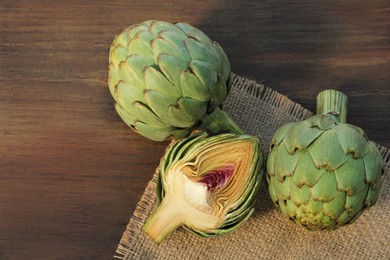 Whole and cut fresh raw artichokes on wooden table, flat lay