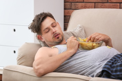 Photo of Lazy man with bowl of chips sleeping on sofa at home