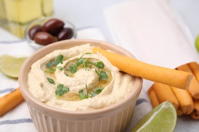 Delicious hummus with grissini sticks on light grey table, closeup