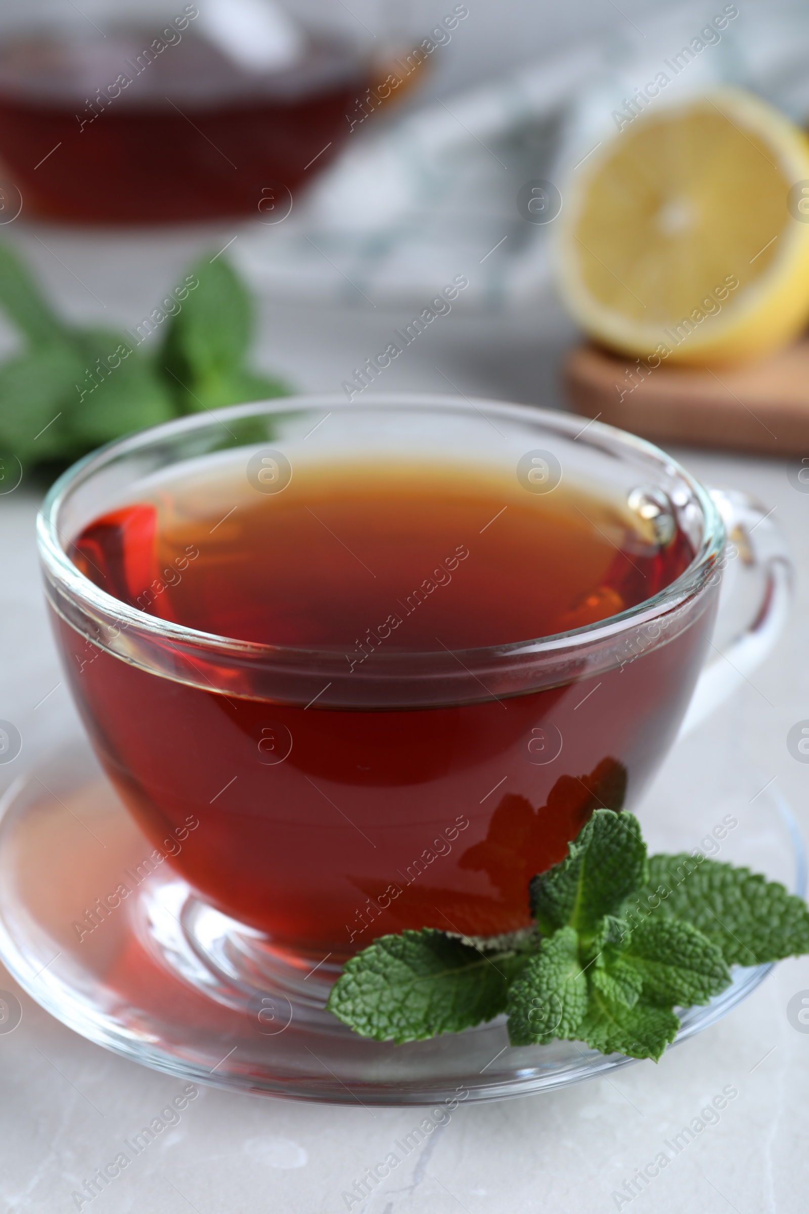 Photo of Cup of hot aromatic tea with mint on light grey marble table