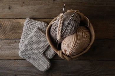 Soft colorful yarns, knitted socks and metal needles on wooden table, flat lay