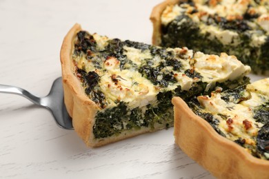 Photo of Taking piece of delicious homemade spinach quiche on white wooden table, closeup